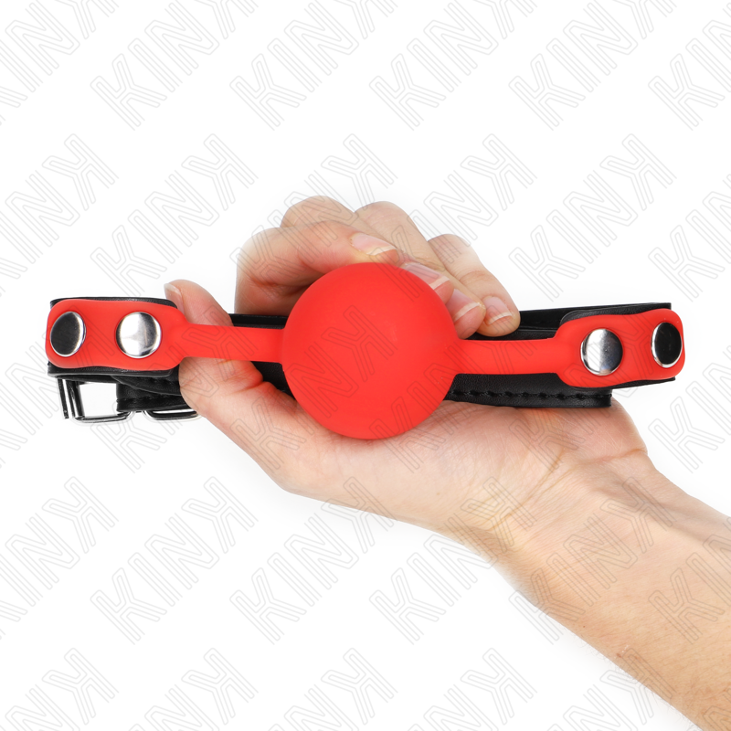 Roter KINK-Ballknebel in einer Hand, mit schwarzem Riemen und Schnalle