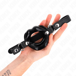 Bâillon lèvres noir brillant posé dans une main, avec sa sangle en simili cuir