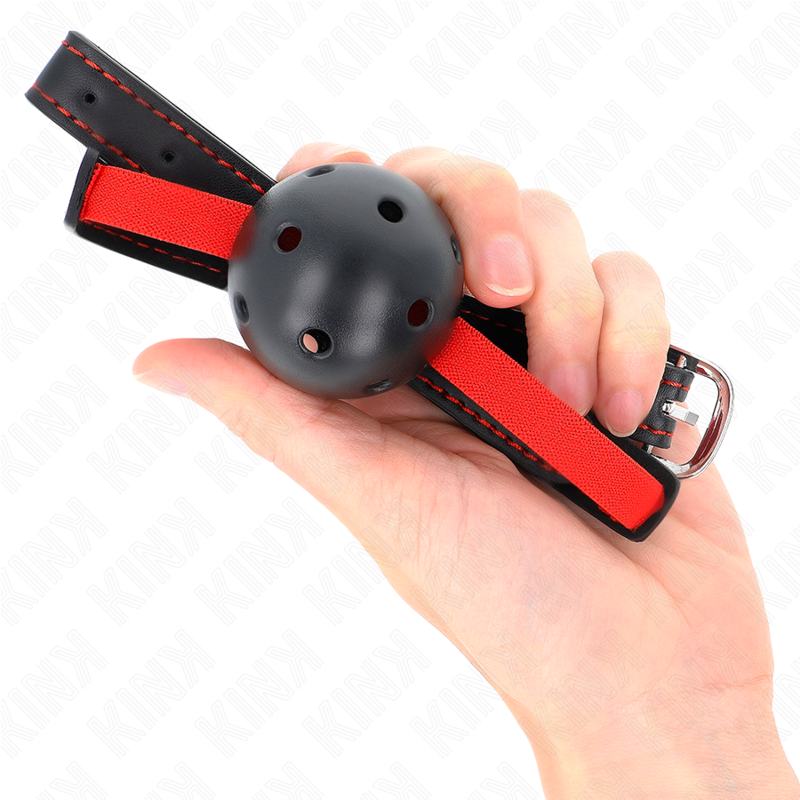 Bâillon à boule noire perforée posé dans une main avec la sangle rouge et noire