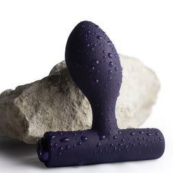 Purple silicone butt plug covered in water droplets on a stone